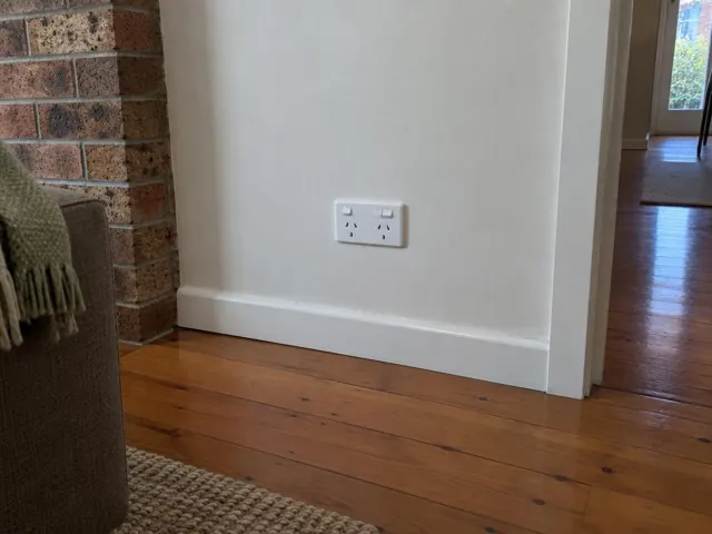 White double power point on a painted wall above timber floorboards and skirting in Cromer